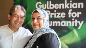 Two people posing in front of a Gulbenkian Prize for Humanity sign